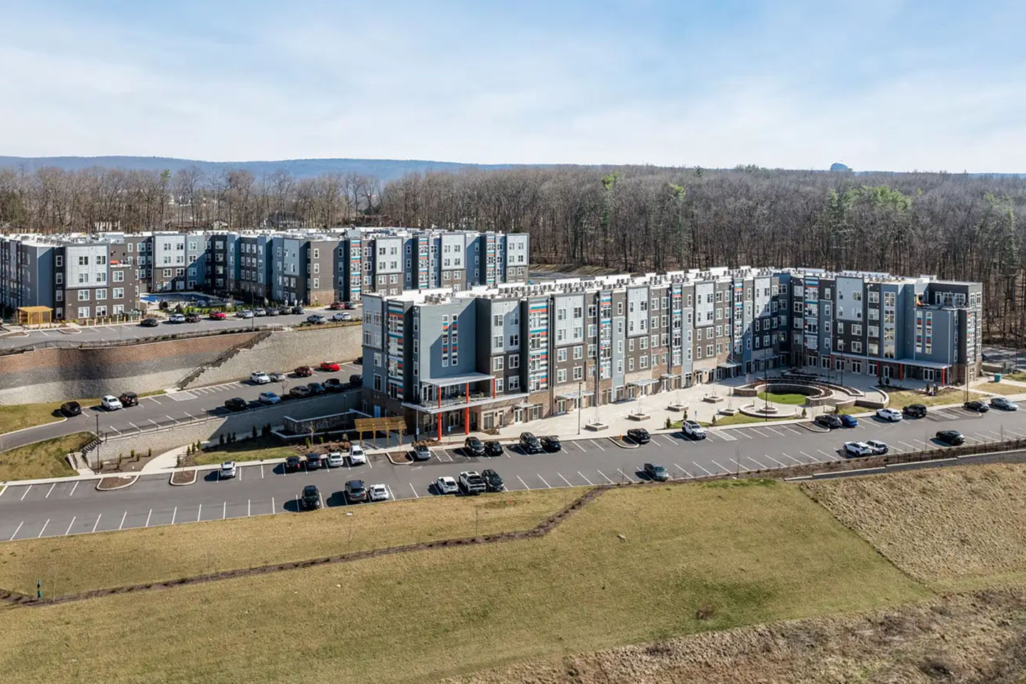 Apartment buildings surrounded by parking lots and walking fields, there also is a forest and a mountain in the distance.